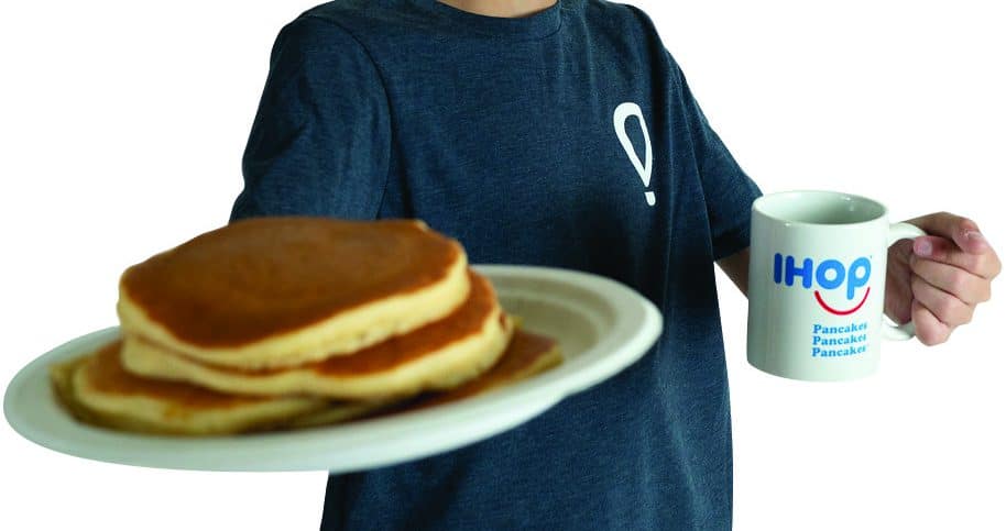 Boy holding pancakes on a plate in one hand and an ihop pancakes cup in other hand